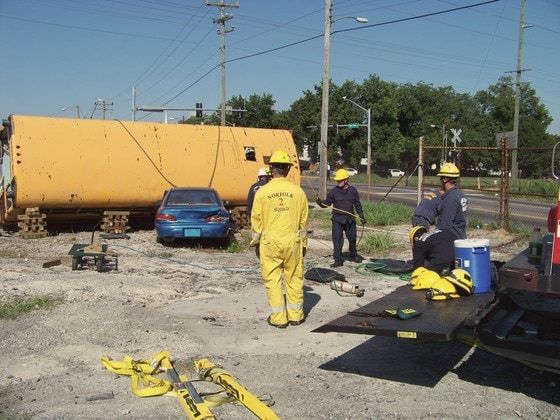Firefighters in yellow gear training on a school bus laid on its side in the GAC yard