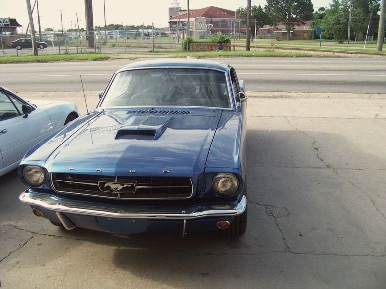 A blue 1965 Mustang fastback parked outside the shop
