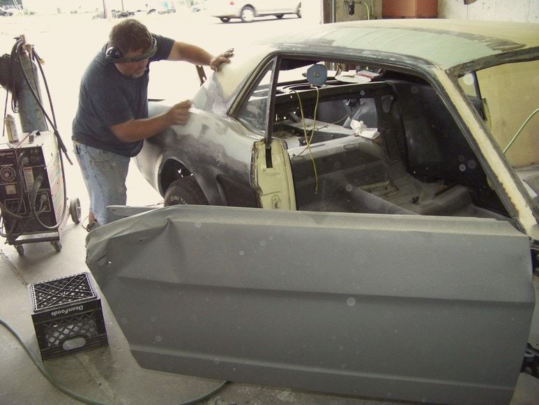 A technician fitting a door on a primered 1965 Mustang