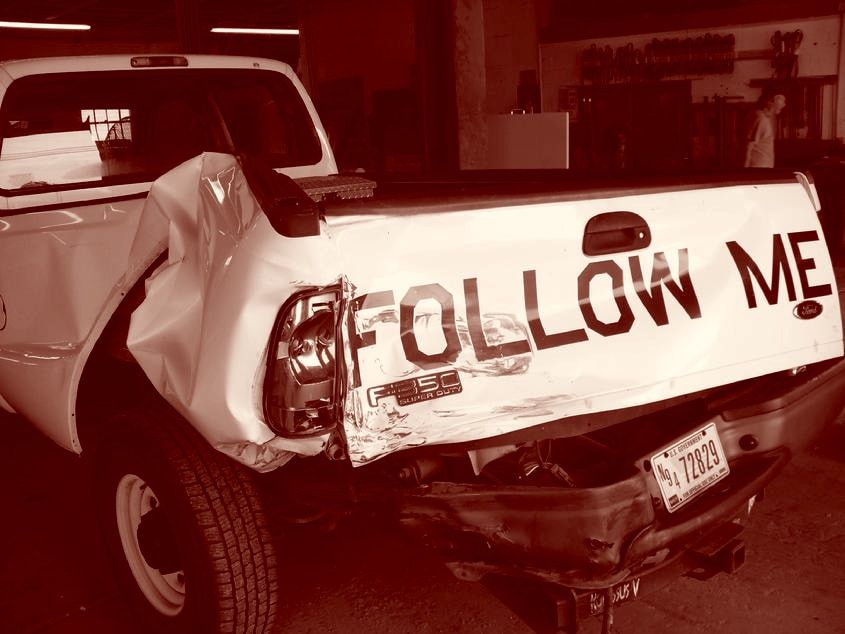 A white Ford F-250 with its rear quarter and tailgate caved in, waiting for repair